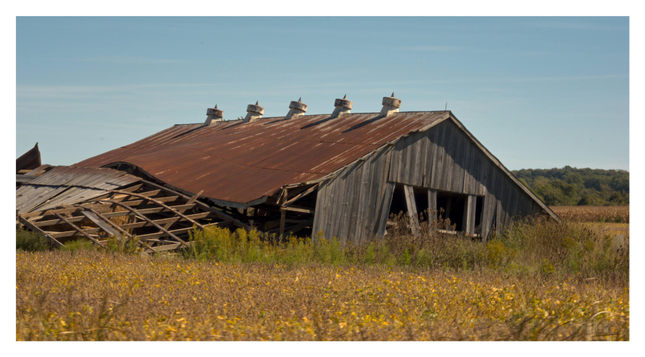 A derelict barn, seemingly decaying and abandoned in a field on a nice summer day.