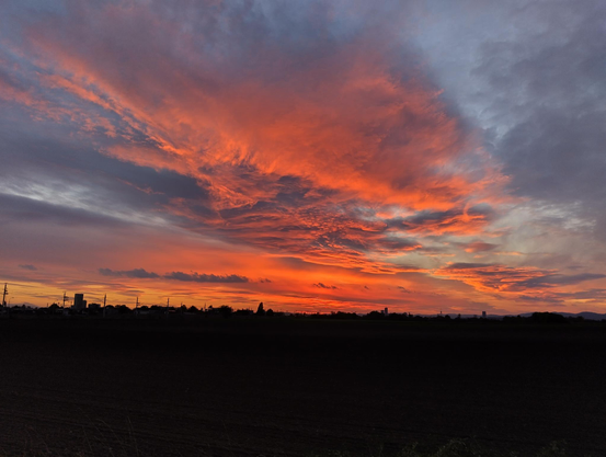 photo dramatically lit clouds - hues of orange, red and violet, and whips of yellow, against a pale pastel blue evening sky