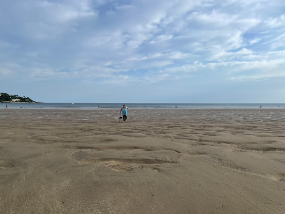 Weiter leerer Strand mit einer einzelnen blaue gekleideten Person darüber blauer Himmel mit einzelnen Wolken