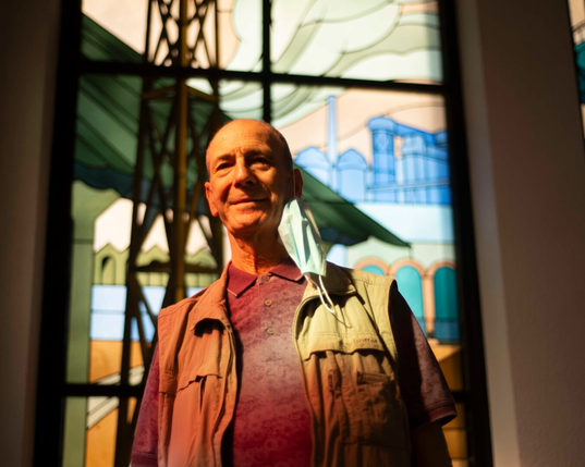 Portrait en contre-plongée d'un ancien ouvrier devant les vitraux, la lumière des vitraux se reflète sur son vissage