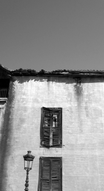 Fotografía en blanco y negro de una casa con las ventanas tapiadas y una farola al aldo