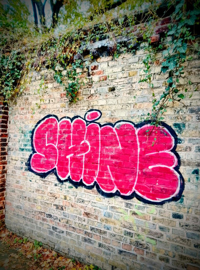 The word shine spray painted in red on a brick wall