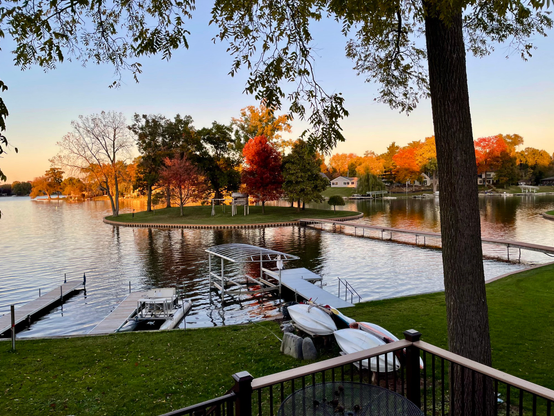 Photograph of a small island with trees on a small lake with more trees on the far shore. The trees have changed colors to yellows and reds. The treetops are illuminated by golden sunset light.
