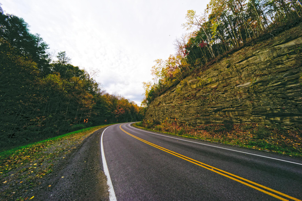 road starts from the lower right and heads diagonally towards the center before curving back to the right past an outcropping of rock covered with trees