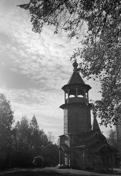 The black-and-white photograph depicts a wooden Orthodox church against a natural backdrop.