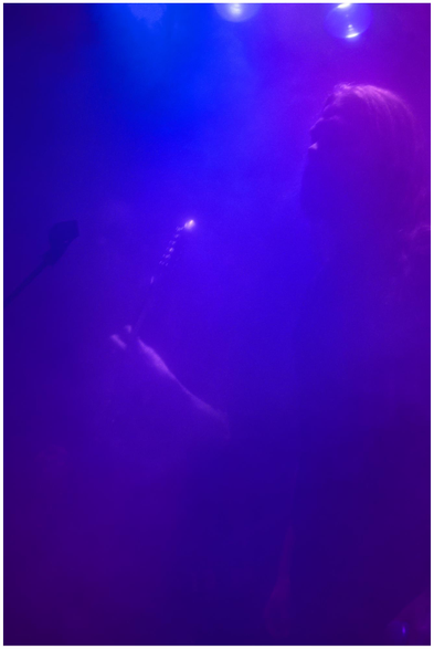 Person spielt Gitarre in blau-violett beleuchtetem Raum mit Nebel.