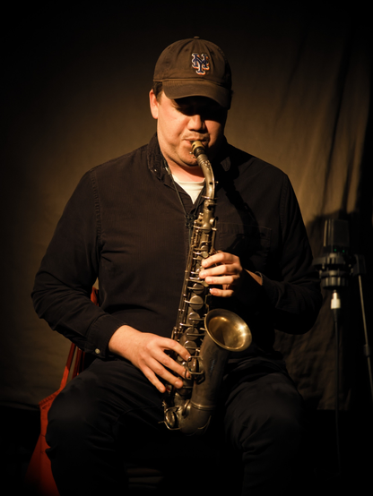Musician playing a saxophone while sitting on a chair.