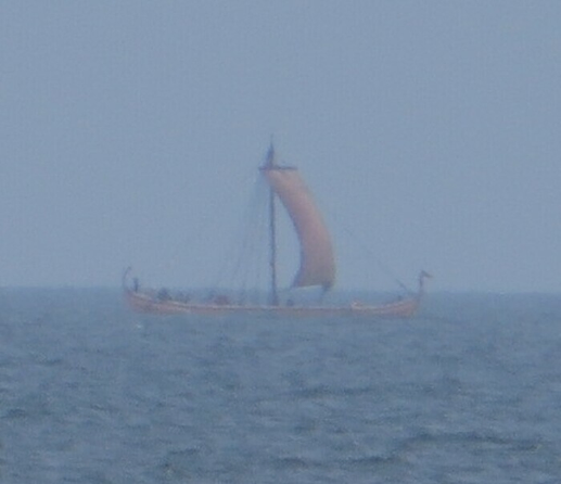 A blurred foto of a distant ship with a square sail passing by. It is the "Helge Ask", a replica of the Skuldelev 5 ship from Vikingeskibsmuseet Roskilde. As close to a real longship as you can get.