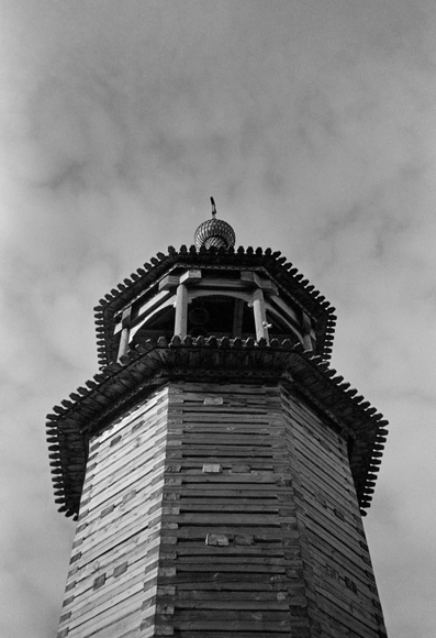 In a black-and-white close-up (from bottom to top), the bell tower of a wooden Orthodox church.
