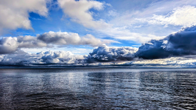 Der Himmel über der See nach einer Regenfront. Es türmen sich Quellwolken vor blauen Himmel auf, der selbst von höheren weißen Wolkenstreifen durchzogen ist. Die kräuselige See reflektiert diesen Himmel.

Das Bild ist in vielen Blau- und Weißtönen.