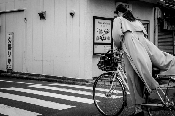 Dona jove en una bicicleta amb la gavardina que voleia cap enrere.