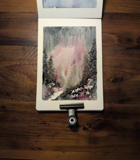 This is an Atmospheric Watercolor Landscape Painting in portrait orientation in an A5 sketchbook using Daniel Smith Rose of Ultramarine, Undersea Green, Payne's Gray, Iridescent Goldstone, and Hansa Yellow Deep. Blue dominates the sides and top, Rose of Ultramarine is dominate in the center, green comes in pops and the yellow and gold are splattered towards the middle to create fireflies. There are dark everywhere trees on the sides for dark contrast and some detail.