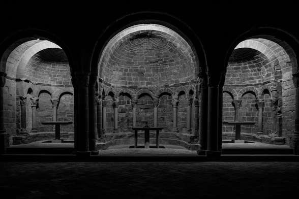 Español: interior en blanco y negro de la iglesia románica del conjunto monumental de San Juan de la Peña, con tres ábsides de piedra iluminados tenuemente. Se aprecian bóvedas semicirculares, columnas con capiteles y tres pequeños altares de piedra.

English: black and white interior of the Romanesque church at the monumental complex of San Juan de la Peña, featuring three softly lit stone apses with semicircular vaults, columns with carved capitals, and three small stone altars.
