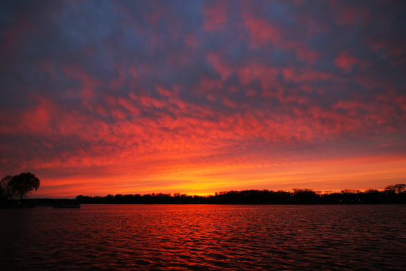Sunset photo of yellow, orange, and red clouds above a lake reflecting the light.