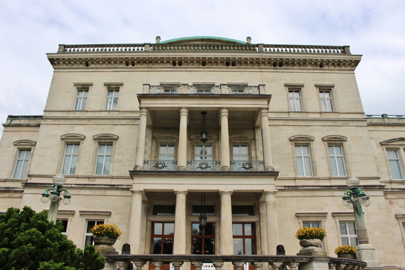 a photo of one of the buildings, from a low perspective, the direct front of it, big columns and windows and pots with flowers 