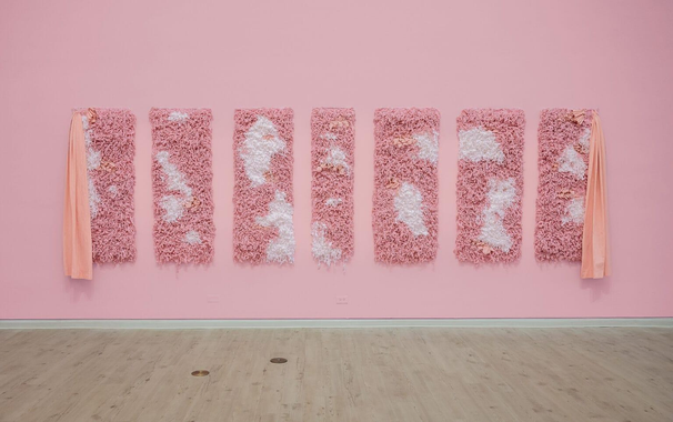 an installation view of 7 fluffy pink and white tapestries by Bryana Bibbs