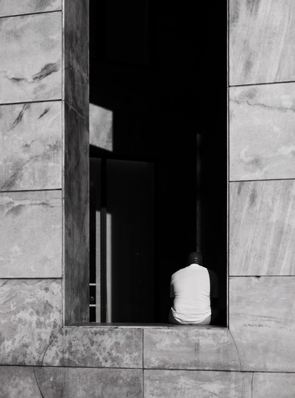 A man is sitting in an opening in a white marble wall.