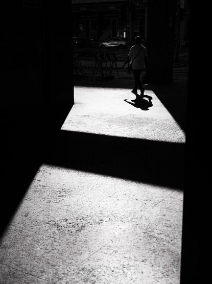 A man walks away in a sunlight patch among shadows.