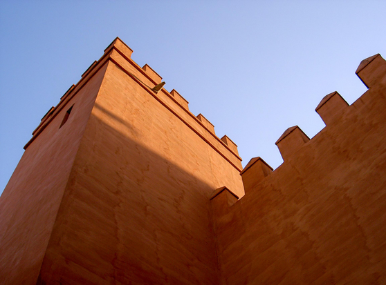 An angled view of the battlements of a terracotta-colored fortress wall against a clear blue sky.