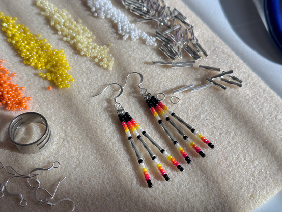 a bead mat covered in jewelry supplies, piles of seed beads, and a pair of beaded drop earrings in black and silver with accents of red, orange, yellow, and white