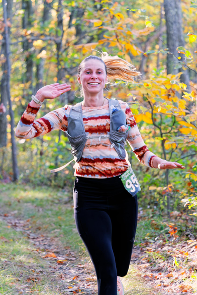 Woman running has her hair in a ponytail off to the right and has her hands pointing the same way.