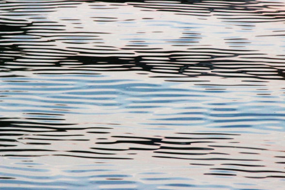 Photograph of light blue and black light reflected on ripples on water forming an abstract pattern of horizontal lines.