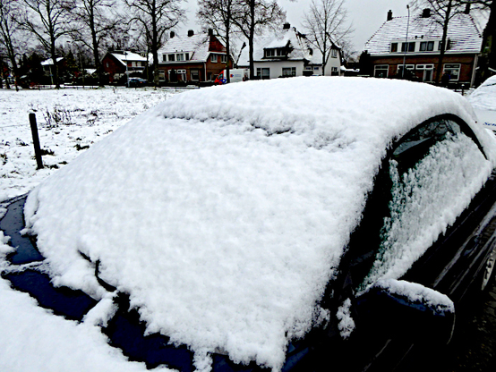 Foto van auto met laag sneeuw op voorruit en motorkap bij besneeuwd veld