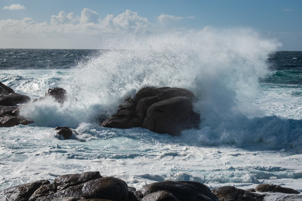 Waves crashing against rocks by the sea under a partly cloudy sky.