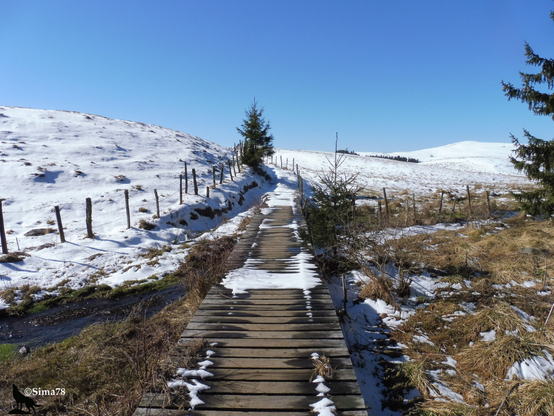 Sentier traversant un paysage de collines enneigées sous un ciel bleu.
Path crossing a landscape of snowy hills under a blue sky.
Sendero que atraviesa un paisaje de colinas nevadas bajo un cielo azul.