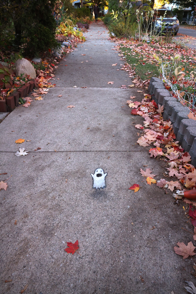 photo of an autumnal sidewalk with a chalk drawing of a very small ghost in the middle of the walkway