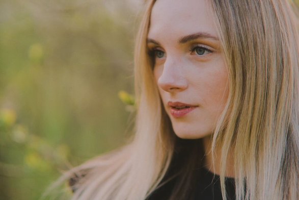 Horizontal portrait of a young woman with light straight hair on a sunny spring evening outdoors.