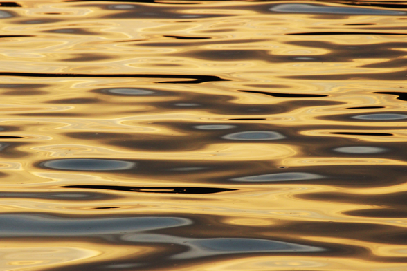 Photograph of sunset light reflected on water forming yellow and brown patterns with light blue ovals.