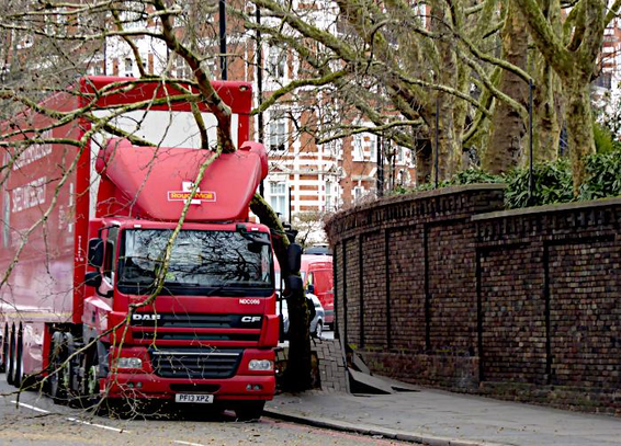 Foto van rode vrachtauto, die een boom op het trottoir heeft omgetrokken