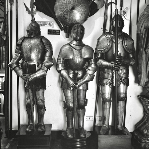 A black-and-white film photo. Three sets of medieval knight’s armour stand side-by-side at the Museo Oro del Perú y Armas del Mundo in Lima, Peru. Saturday, September 20, 2025.