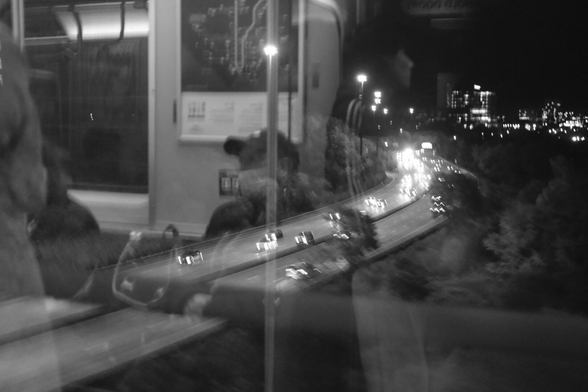 Night. Looking from the subway car window down at the Don Valley and the parkway. There are lights of traffic and the reflection of the subway car interior in the glass, making an almost ghostly overlay of the valley below