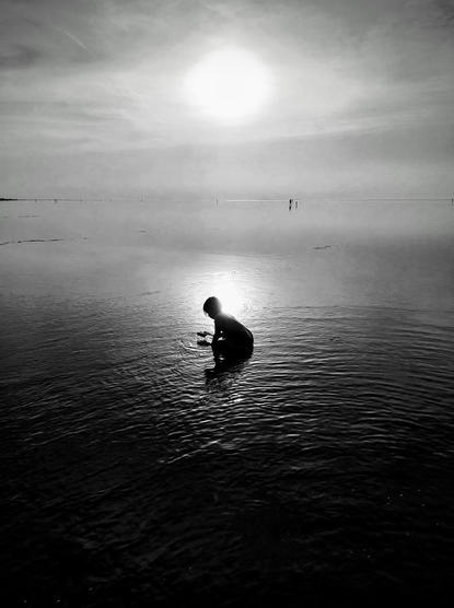silhouettes of playing kid against setting sun mirrored on wet mud flat