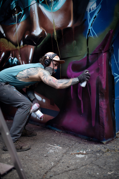 A spraycan artist working on a mural depicting a stylized female face.