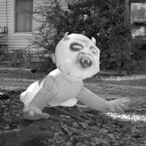 A black-and-white film photo. A giant inflatable baby with devil horns is stationed in front of a house in East Austin, Texas. Monday, October 20, 2025.