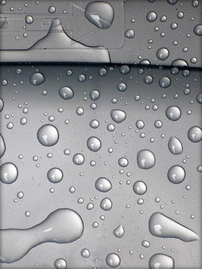 A colour photograph showing standing water droplets on the lid of a recycling bin. The droplets sit on a silvery grey background with the frame split towards the top by a gently arcing horizontal line and an arrow points right at the very top of the frame.