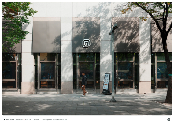 규칙적으로 난 건물 안 카페의 창문과 길고 가는 회색 차양 가운데 위치한 커피앳웍스의 로고.