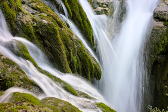 Fotografía del detalle de una cascada en larga exposicion, el agua fluye en varias direcciones entre las rocas cubiertas de musgo.