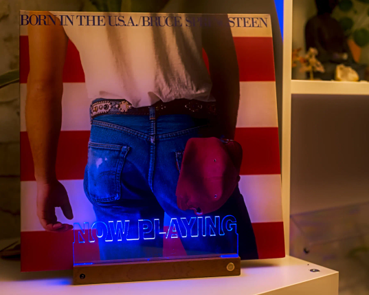 Das Cover von "Born in the USA" zeigt einen Männerrücken in weißen Shirt und Jeans. Ein schwerer Gürtel in der Hose, eine rote SChirmmütze in der Hosentasche, vor dem rotweißen Streifenbanner. 