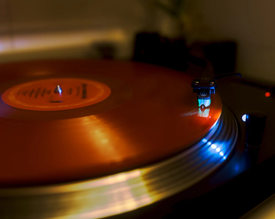 Eine orange Schallplatte liegt auf einem Plattenteller. Sie dreht sich, der Tonarm liegt noch am Anfang der Platte. 