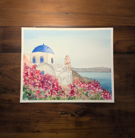 This is a watercolor landscape painting of Greece in landscape orientation on Arches Coldpress watercolor paper.  The sky is a pale blue gradient. On the right there is a  landmass at the horizon line and then a triangle of turquoise sea. Over looking the ocean are some structures some are terracotta but most are white. The domed roof is the classic Greek  blue. The structures have pink and purple flowers growing around them.