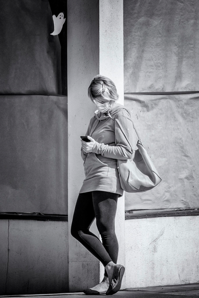 Small paper ghost in window appears to call down to a woman standing on the corner looking at her phone in San Francisco.