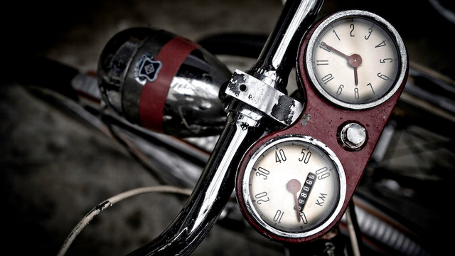 Auf dem Foto ist ein Tacho und eine analoge Uhr zu sehen die an einem Lenker befestigt sind. Im Hintergrund sieht man den alten Frontscheinwerfer.