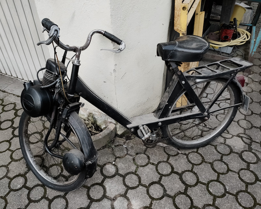 Das Bild zeigt eine Velo Solex auch nur Solex genannt. Sie steht an der Ecke einer Garage die offen ist.