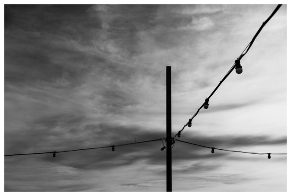 Lichterketten hängen vor einem sich zuziehenden Himmel. Schwarzweißbild.