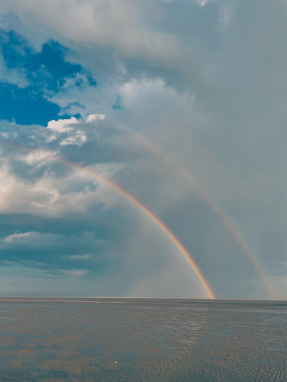 Morgendliches Watt mit doppeltem Regenbogen und Wolken