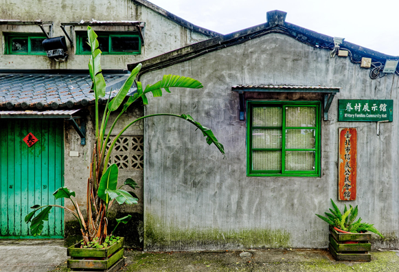 Facades of historical one- and two-storey buildings with potted plants in the foreground; a sign in English and Chinese reads “Military Families Community Hall.”